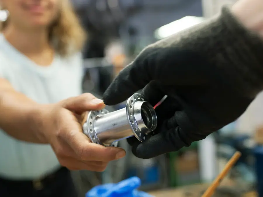 A close up of a technician handing her colleague a bike part while working together in a bicycle workshop.