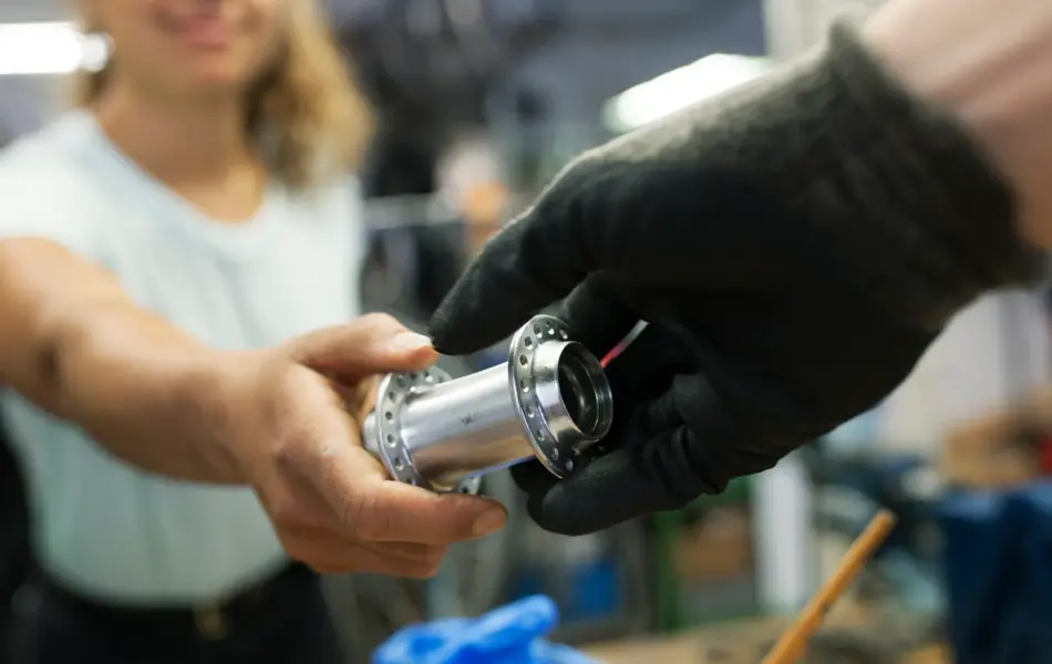 A close up of a technician handing her colleague a bike part while working together in a bicycle workshop.