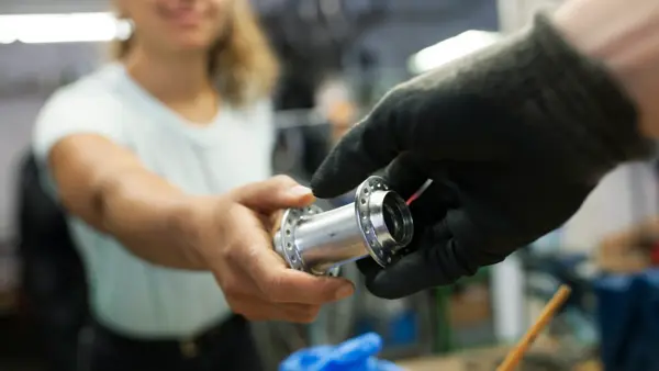 A close up of a technician handing her colleague a bike part while working together in a bicycle workshop.