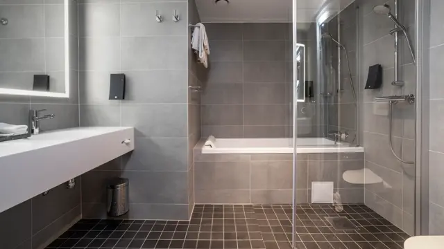 Badekar, grå gulvfliser, grå veggfliser, dusj, vask, speil, toalett