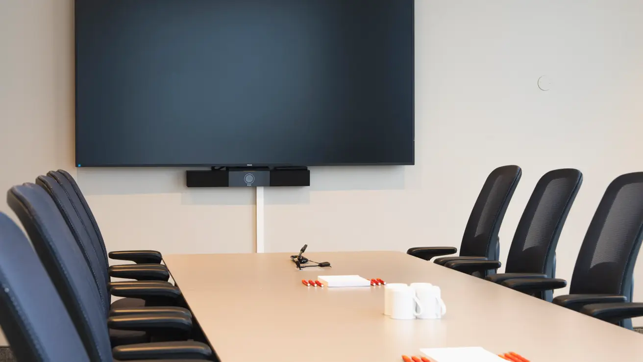 Nærbilde av TV skjerm, langbord og stoler i møterom