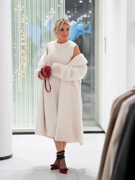 Dame med hvit kåpe, hvit kjole, rød veske, røde pumps, sorte nylonstrømer