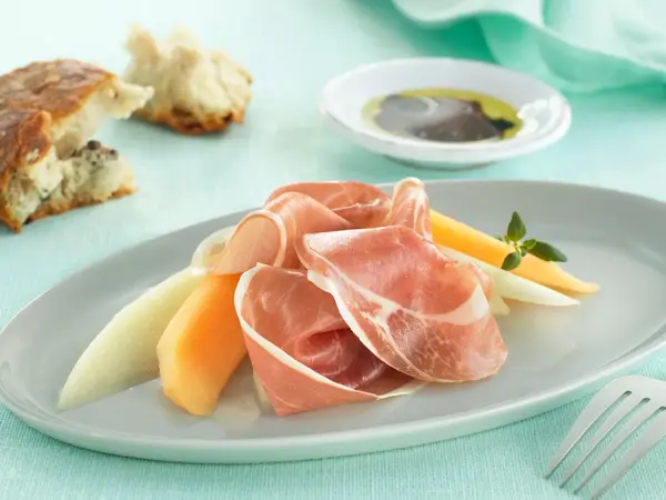 Melom og serranoskinke på tallerken på turkis duk