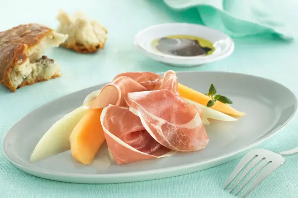 Melom og serranoskinke på tallerken på turkis duk