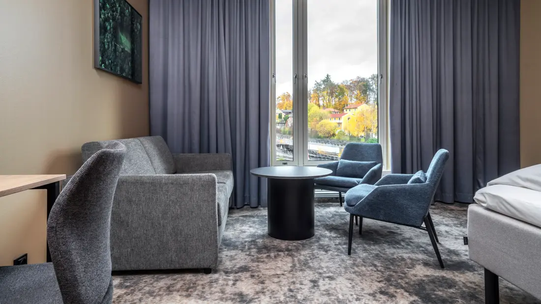 Businessrom med sittegruppe, vegghengt TV, gardiner, utsikt og teppegulv