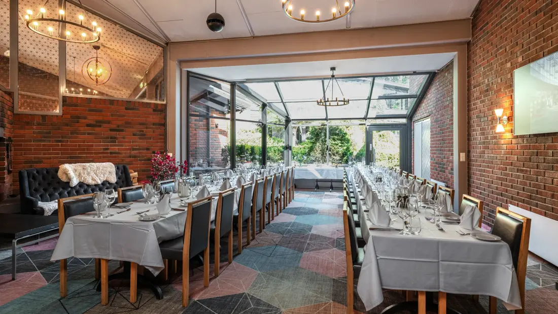 To langbord dekket til selskap i eget lokale, med murvegger på siden og stor glassvegg i enden. Lysekroner i taket,