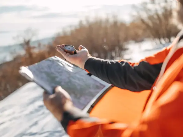 Mann holder kart og kompass i snødekt landskap
