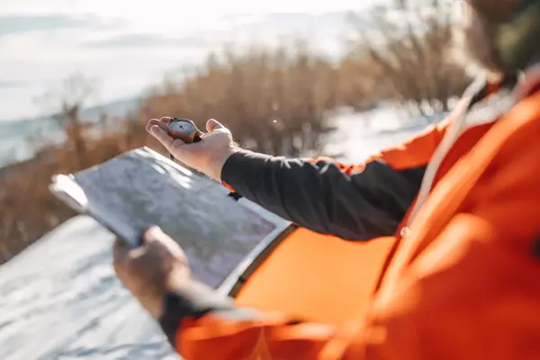Mann holder kart og kompass i snødekt landskap