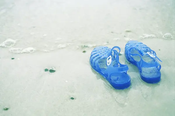 Blå gummisko med glitter i vannkanten på strand