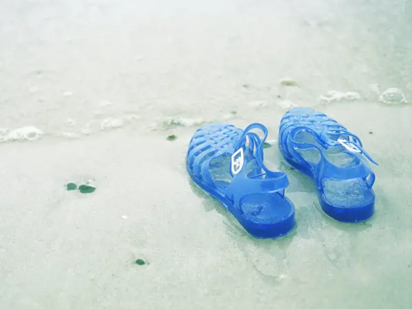 Blå gummisko med glitter i vannkanten på strand