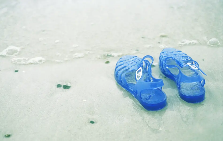 Blå gummisko med glitter i vannkanten på strand