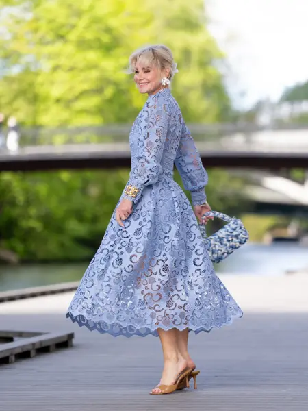 Dame i lange dueblå kjole, liten veske og sandaler.