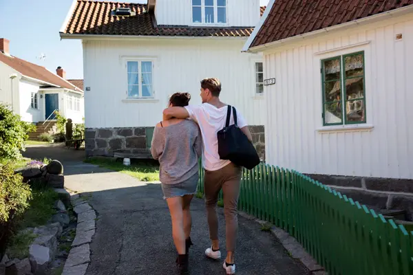  Mann med hvit t-skjorte og beige chinos holder rundt dame mens de vandrer opp gate, sett bakfra 