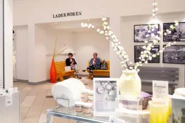 Interiørutstilling foran to damer sittende på benker i Ladekroken på AMFI Voss