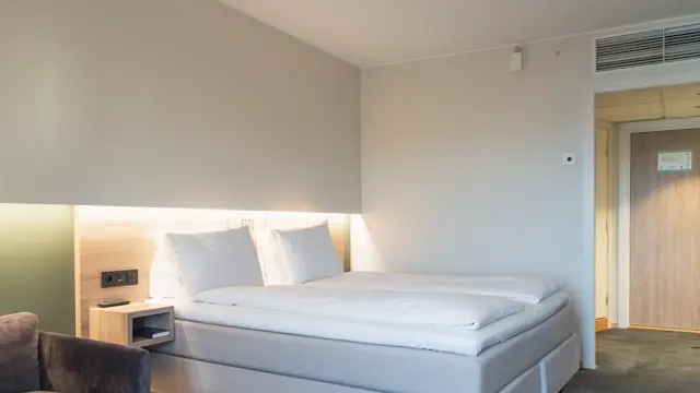 Businessrom med dobbeltseng, hvitt sengetøy, og nattbord i lyst tre.