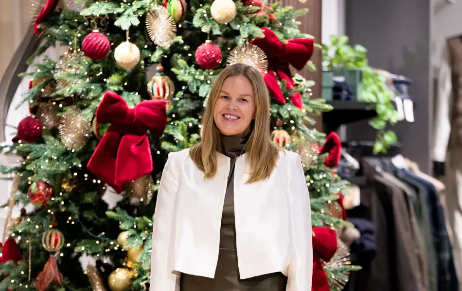 Dame med hvit jakke, sort høyhalset genser, brunt satengskjørt og sandaletter med strass.