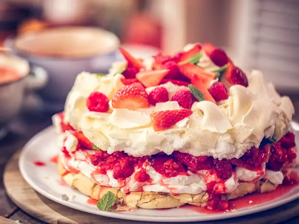 Delicious Berry Pavlova Cake with fresh strawberries, raspberries, mint leaves and whipped cream.