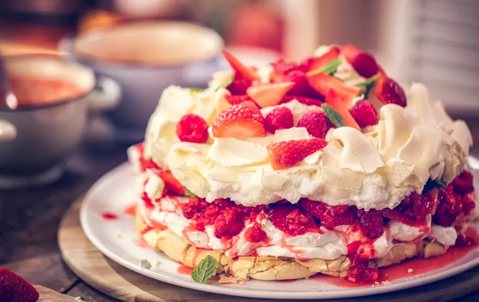 Delicious Berry Pavlova Cake with fresh strawberries, raspberries, mint leaves and whipped cream.