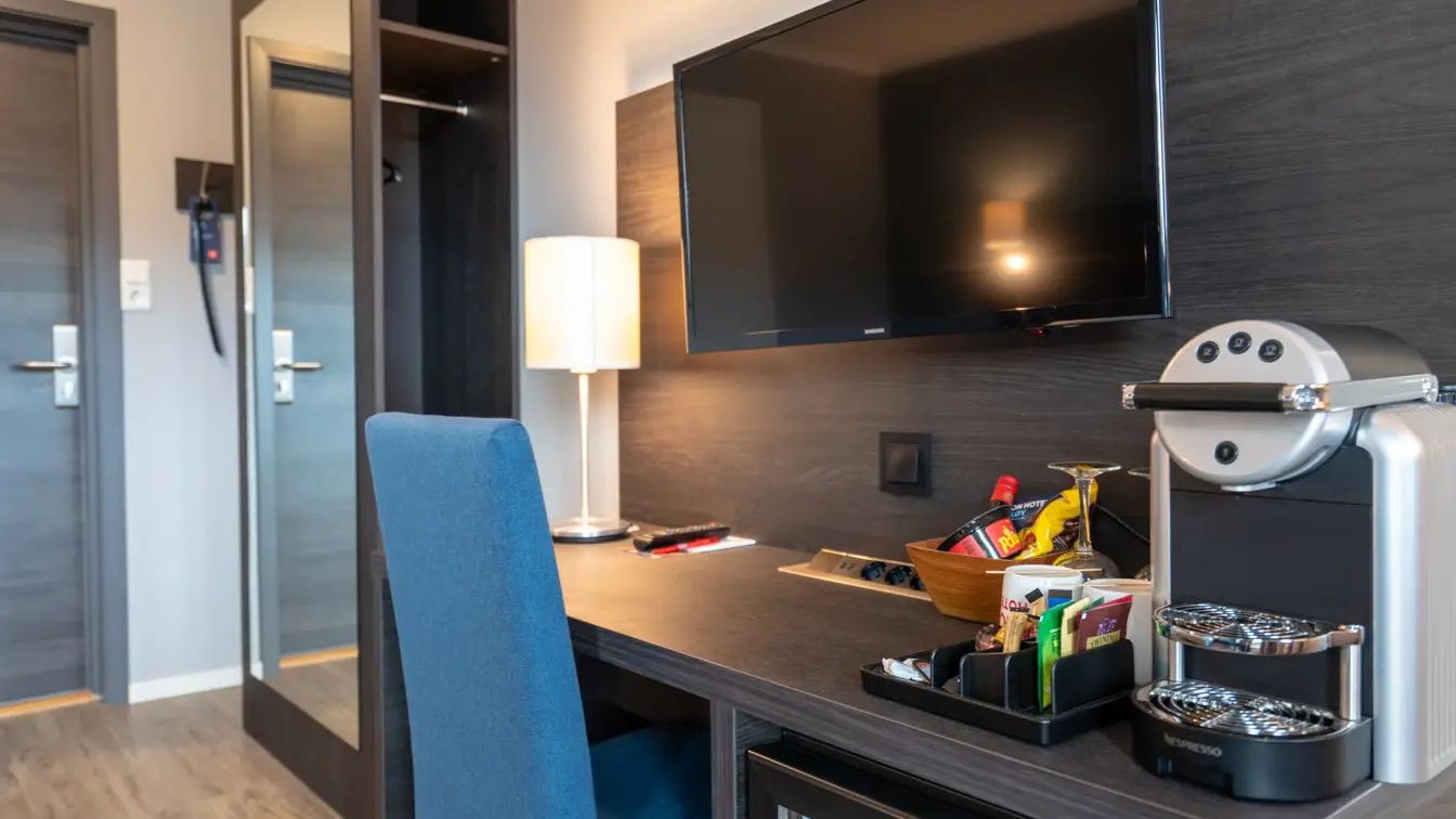 Skrivebord, blå stol, TV, kaffemaskin, speil på veggen