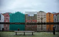 Utsnitt av Kjøpmannsgata som speiler seg i Nidelva, med nr. 15 i midten. I forgrunnen en benk.