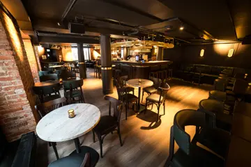 Brune bord med tilhørende brune stoler og sofa. Lyse marmorbord med tilhørende brune stoler. Brun vegg på én side, mursteinsvegger på resterende. Parkettgulv.