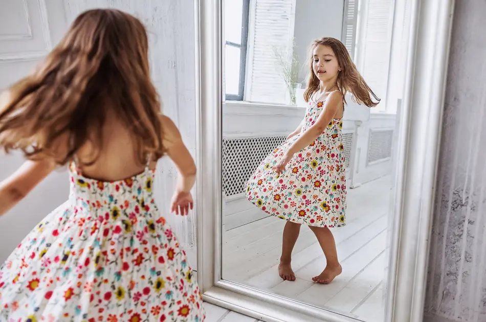lovely smiling little girl about 6-10 years old on the floor in cute flower summer dress smiling  turning around at the mirror