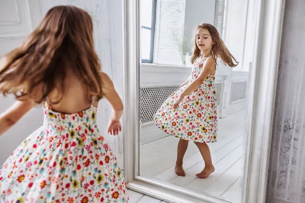 lovely smiling little girl about 6-10 years old on the floor in cute flower summer dress smiling  turning around at the mirror