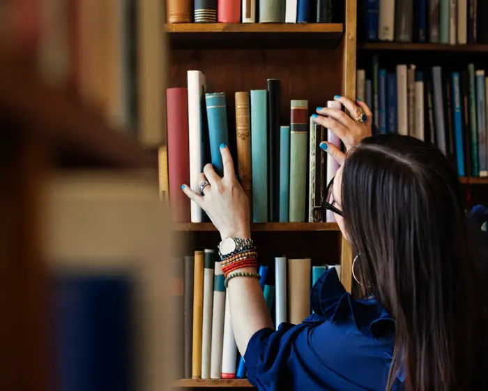 Dame leter etter bok i bokhylle