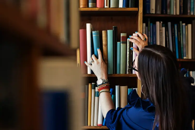 Dame leter etter bok i bokhylle