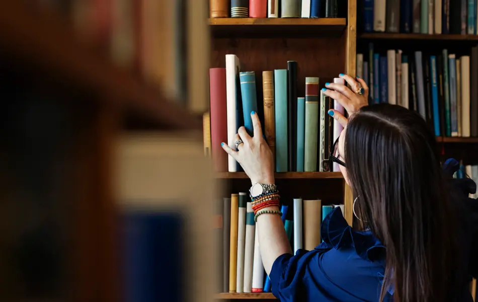 Dame leter etter bok i bokhylle