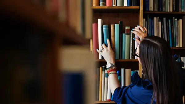 Dame leter etter bok i bokhylle