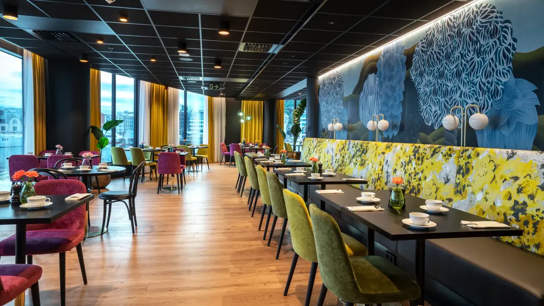 Tapetvegg i mønster, spisebord, grønn stol, gul sofa, vindu, runde spisebord 