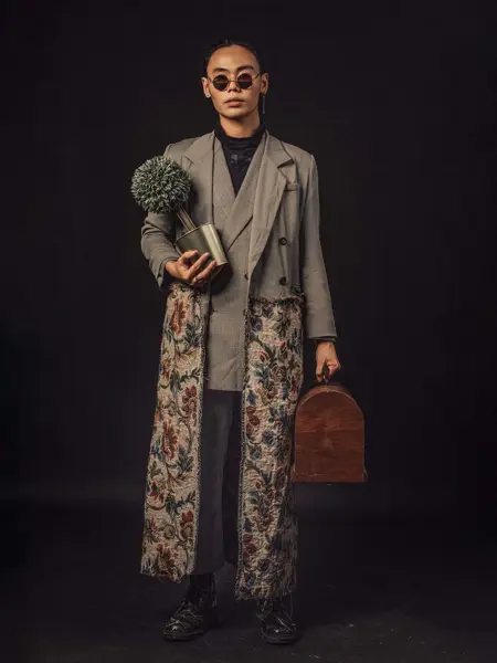 En asiatisk kinesisk mann som bærer en plante og en kortveske som ser på kamera med full kroppslengde med solbriller