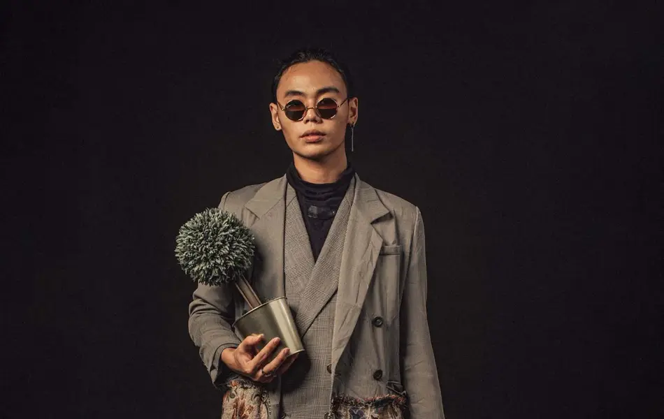 En asiatisk kinesisk mann som bærer en plante og en kortveske som ser på kamera med full kroppslengde med solbriller