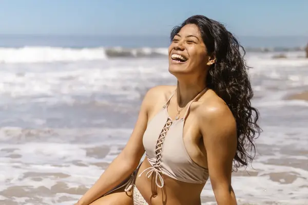 Dame som smiler og sitter på badestranden