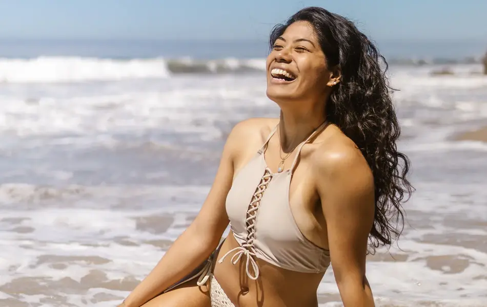 Dame som smiler og sitter på badestranden