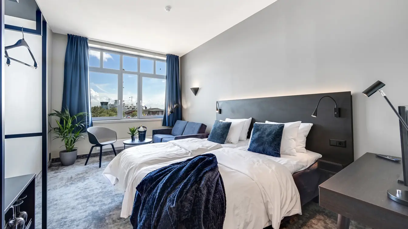 Dobbeltseng, hvite vegger, vindu, blå gardiner, skrivebord, skap