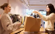 Ansatt rekker en handlepose til en kunde i en bruktbutikk