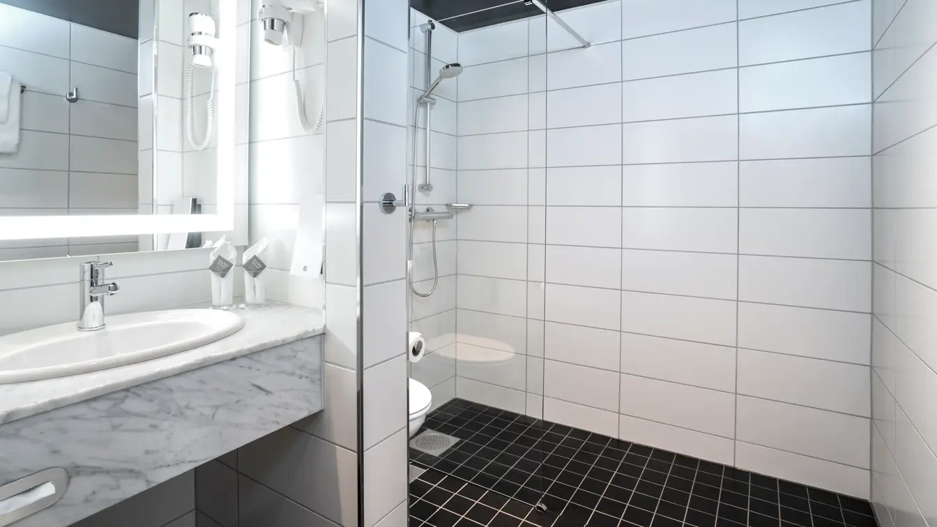 To enkeltsenger, blomstret tapet bak sengene, gul stol, arbeidspult og store vinduer med store gule gardiner på twin room på Thon Hotel Cecil i Oslo sentrum