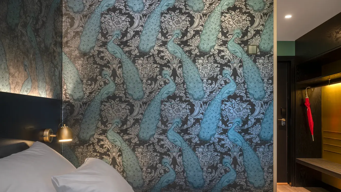 Seng, tapetvegg med mønster, parkettgulv. 