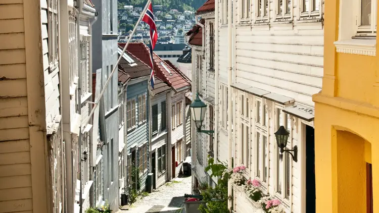 Et smug i gamlebyen i Bergen med norsk flagg og sol som skinner