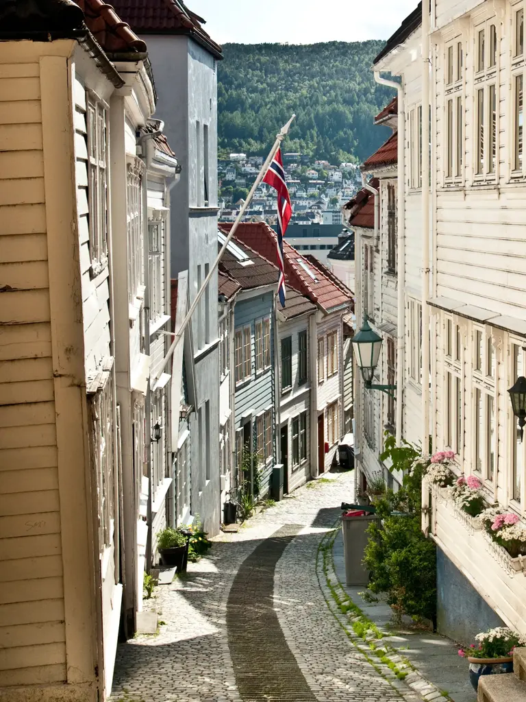 Et smug i gamlebyen i Bergen med norsk flagg og sol som skinner