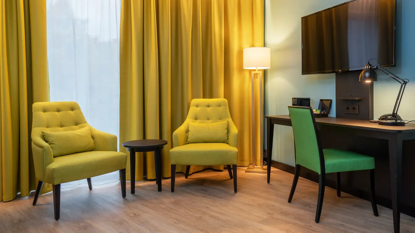 Sittegruppe med gule stoler, gule gardiner, skrivebord med grønn stol og TV i business rom på Thon Hotel Linne