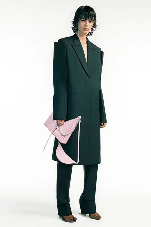 Dame med kort mørkthår og en sort lang dressjakke med store skuldre og en rosa håndveske 