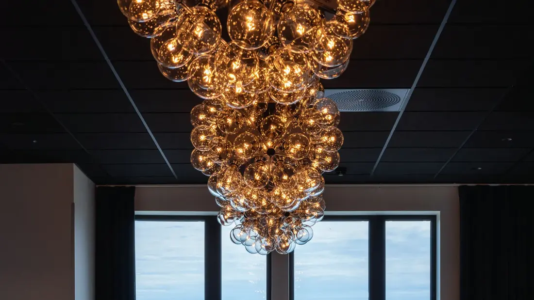 Sort tak med vegghent lysekrone, stort vindu med utsikt over hustak. På Thon Hotel Norge i Kristiansand. 