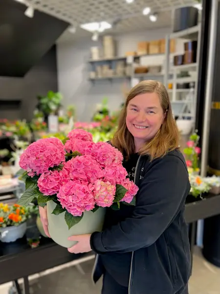 Dame holder rosa blomster i grønn potteplante