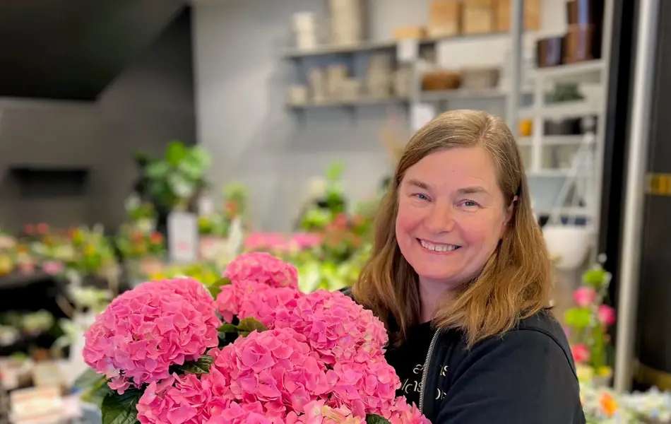 Dame holder rosa blomster i grønn potteplante