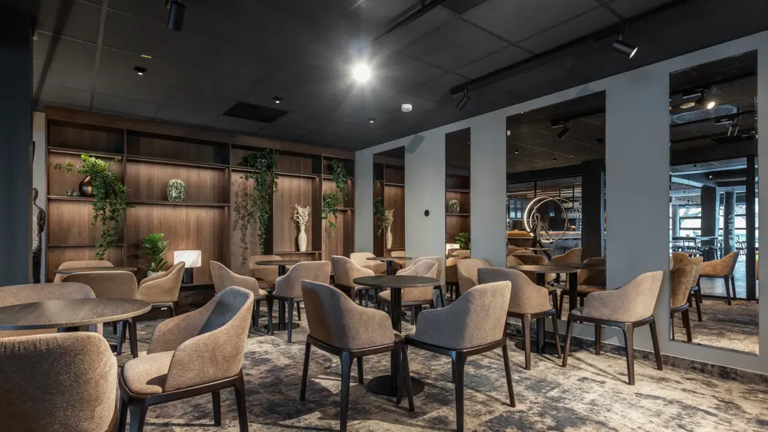 Lite møterom med teppegulv, store speil på veggen. Stoler rundt små svarte cafebord.