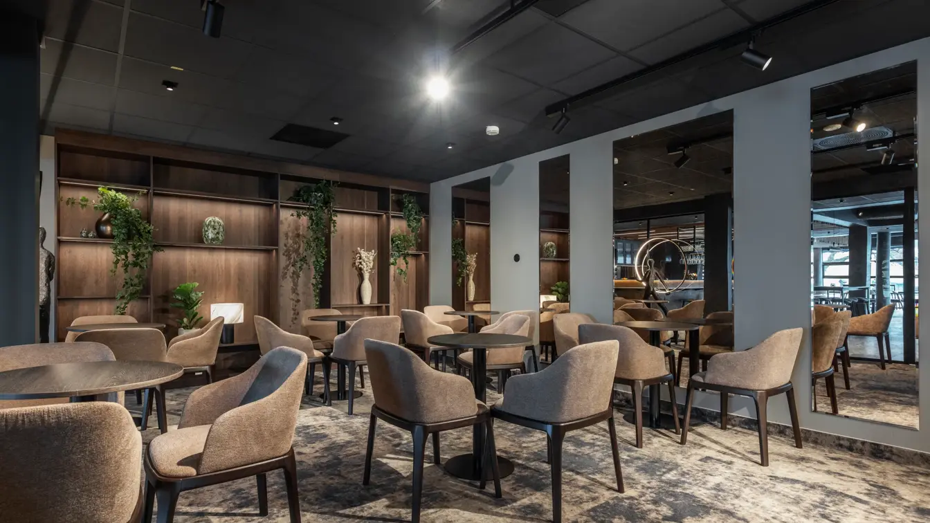 Lite møterom med teppegulv, store speil på veggen. Stoler rundt små svarte cafebord.