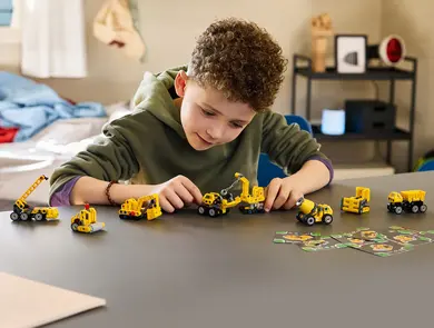 Barn leker med gule LEGO Technic-anleggsmaskiner på et bord.
